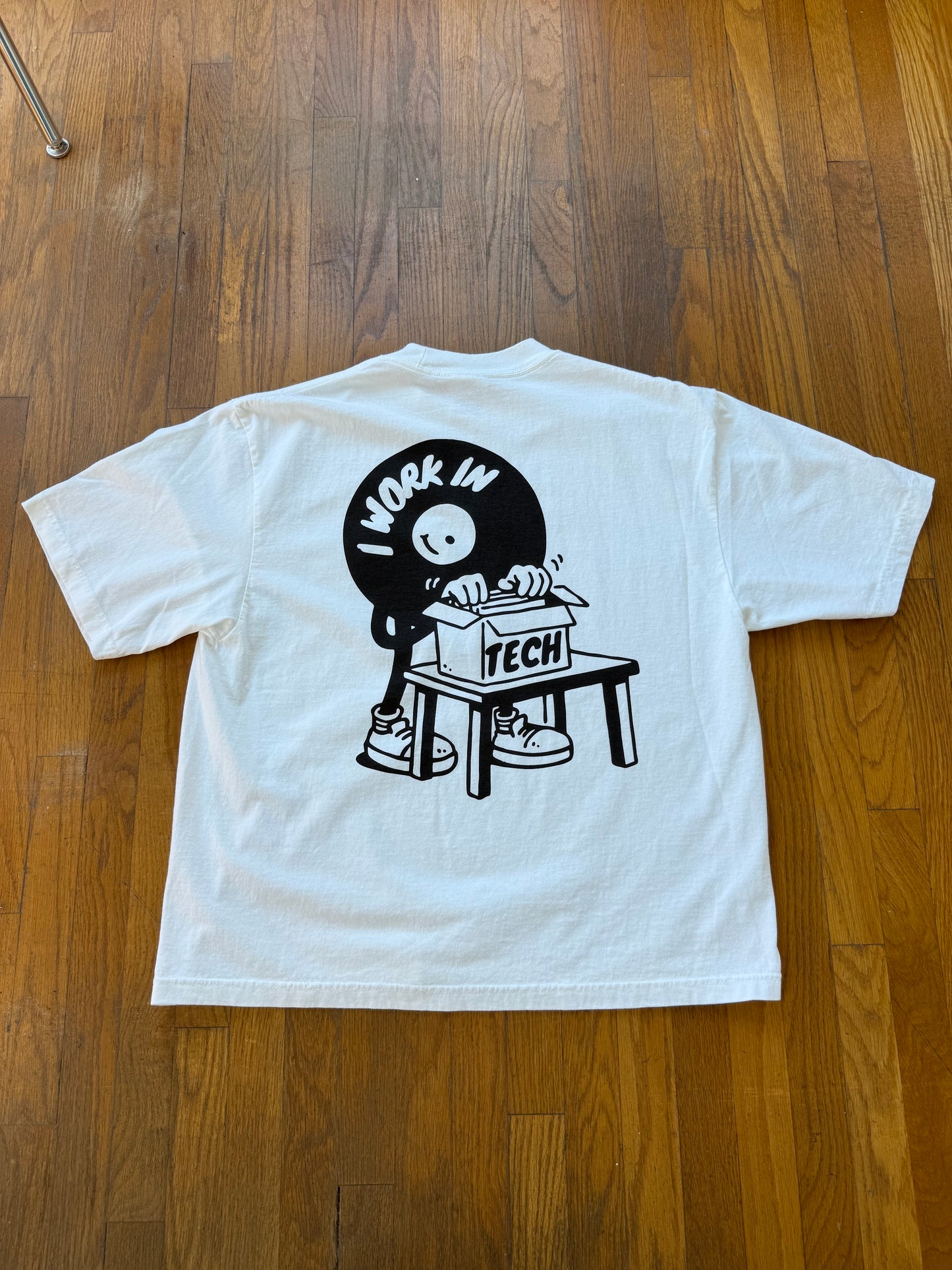 White t-shirt with black graphic design on a wooden floor